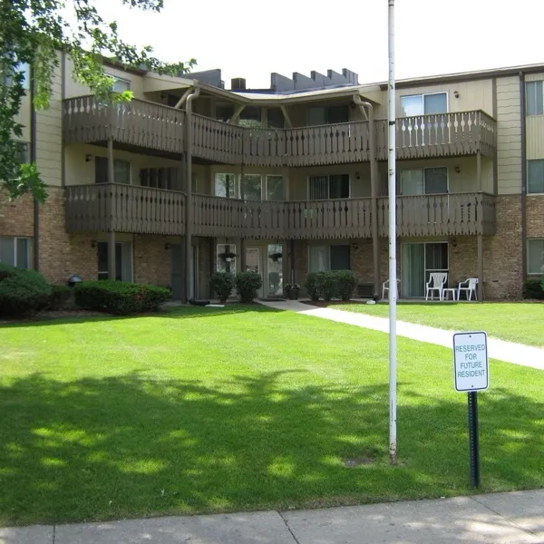 Front of the three-storey brick apartment building with wooden balconies and lawn